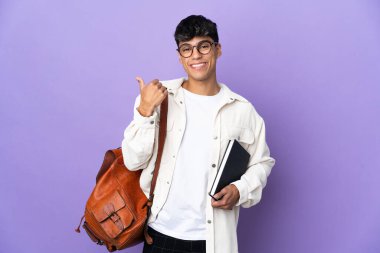Young student man over isolated purple background pointing to the side to present a product