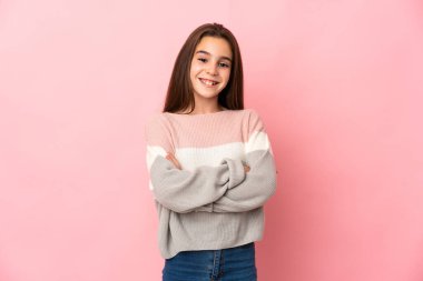 Pembe arka planda izole edilmiş küçük bir kız kollarını ön tarafta kavuşturuyor.