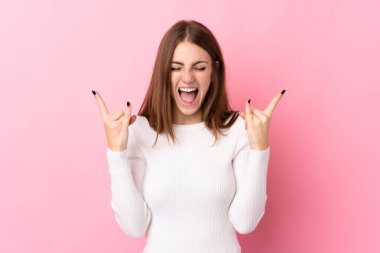 Soyutlanmış pembe arka planda genç bir kadın kaya jesti yapıyor