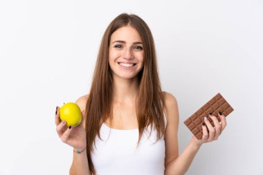 Bir elinde çikolata tableti, diğer elinde elma olan izole edilmiş beyaz arka planda genç bir kadın.