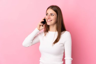 İzole edilmiş pembe arka planı olan genç bir kadın cep telefonuyla sohbet ediyor.