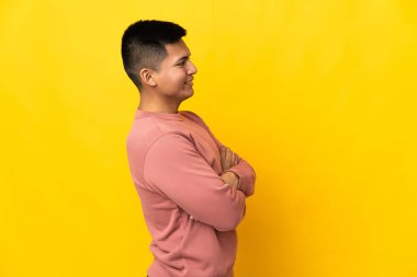 Genç Ekvadorlu adam sarı arka planda yalıtılmış, yan pozisyonda.