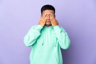 Genç Ekvadorlu adam mor arka planda izole edilmiş gözleri elleriyle kaplayan