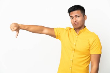 Beyaz arka planda izole edilmiş genç Ekvadorlu adam, olumsuz ifadelerle baş parmağını aşağı gösteriyor.