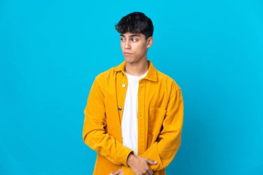 Soyutlanmış mavi arka planda genç bir adam şüpheli hareketler yapıyor.