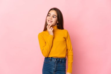 Küçük kız pembe arka planda soyutlanmış gülümserken yukarı bakıyor