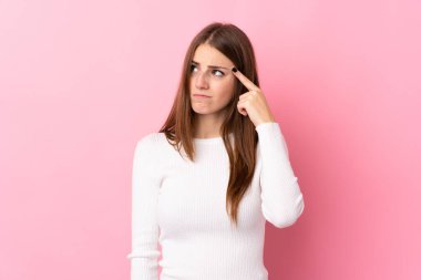 Soyutlanmış pembe arka planda genç bir kadın deliliğin jestini yapıyor. Parmağını kafaya koyuyor.