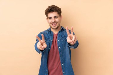 Caucasian man isolated on beige background smiling and showing victory sign