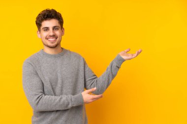 Kafkasyalı genç adam arka planı izole etti. Davet etmek için ellerini yana uzattı.