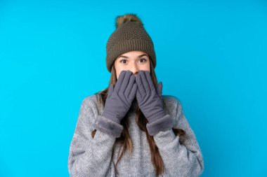 Kışlık şapkalı genç bir kız izole edilmiş mavi bir arka plan ve şaşırtıcı bir yüz ifadesi var.