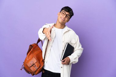 Young student man over isolated purple background shaking hands for closing a good deal