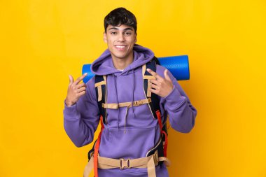 Young mountaineer man with a big backpack over isolated yellow background giving a thumbs up gesture