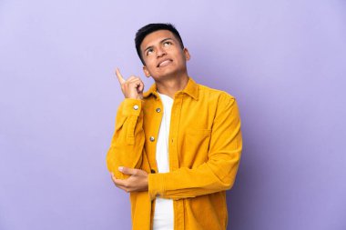 Genç Ekvadorlu adam mor arka planda izole edilmiş. Harika bir fikre işaret ediyor.