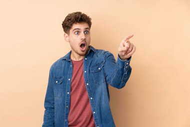 Caucasian man isolated on beige background pointing away