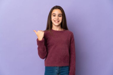 Mor arka planda izole edilmiş küçük bir kız bir ürünü sunmak için yan tarafı işaret ediyor.