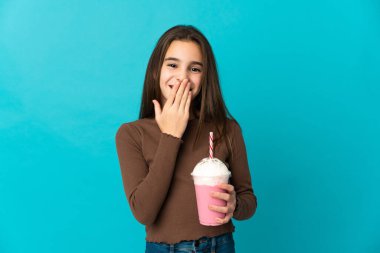 Mavi arka planda izole edilmiş çilekli milkshake 'li küçük kız mutlu ve gülümsüyor.