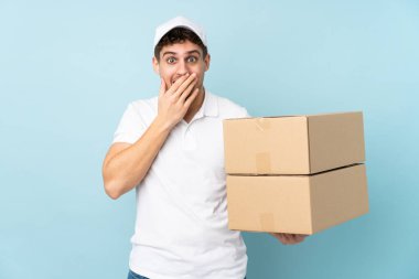 Teslimatçı beyaz adam mavi arka planda izole edilmiş, şaşırmış yüz ifadesi var.