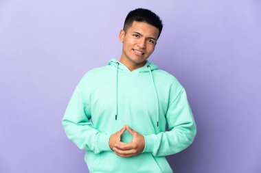 Genç Ekvadorlu adam, mor arka planda izole edilmiş gülüyor.