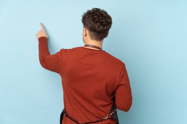 Hairdresser caucasian man isolated on blue background pointing back with the index finger