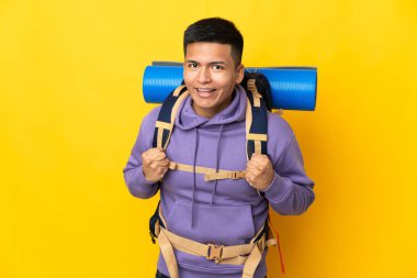 Sarı arka planda saklanmış büyük sırt çantalı genç dağcı galibiyeti kutluyor.