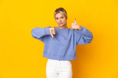 Young Russian woman isolated on yellow background making good-bad sign. Undecided between yes or not