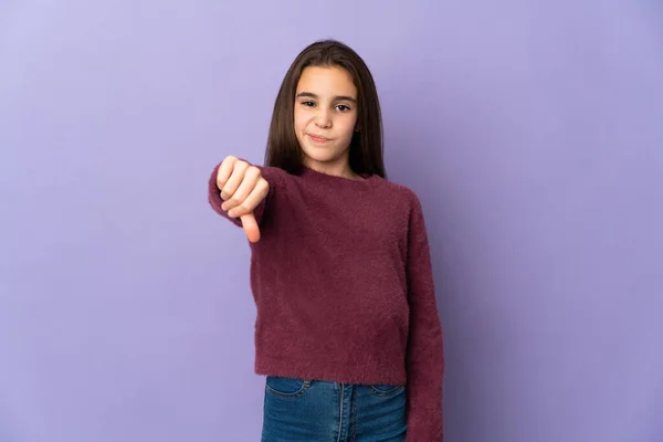 紫色の背景に孤立した少女は否定的な表現で親指を示しています — ストック写真