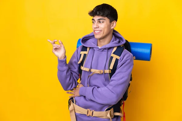 Молодий Альпініст Великим Рюкзаком Над Ізольованим Жовтим Тлом Спрямованим Пальцем — стокове фото