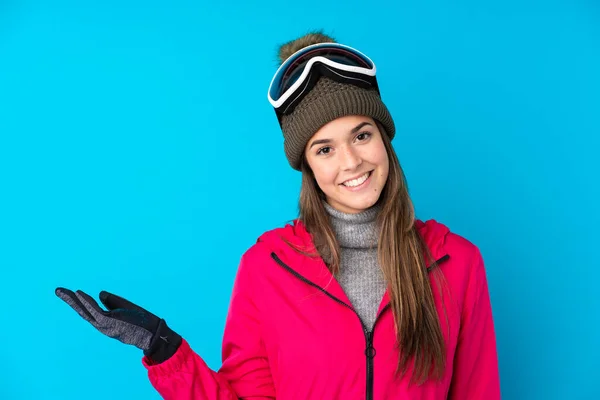 Nastoletnia Narciarka Okularach Snowboardowych Odizolowanym Niebieskim Tle Trzymająca Wyimaginowaną Przestrzeń — Zdjęcie stockowe