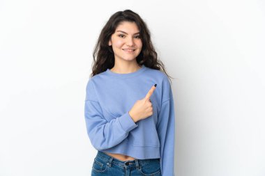 Beyaz arka planda izole edilmiş genç Rus kız bir ürünü sunmak için kenarı işaret ediyor.