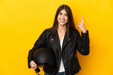 Sarı arka planda motosiklet kaskı tutan beyaz bir kadın harika bir fikre işaret ediyor.