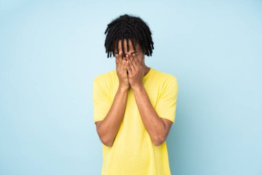 Genç Afrikalı Amerikalı adam mavi arka planda izole edilmiş, yorgun ve hasta bir ifadeyle.