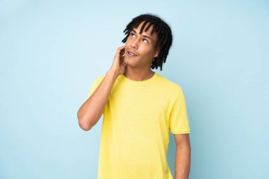 Genç Afrikalı Amerikalı bir adam mavi arka planda izole edilmiş bir fikir düşünüyor.