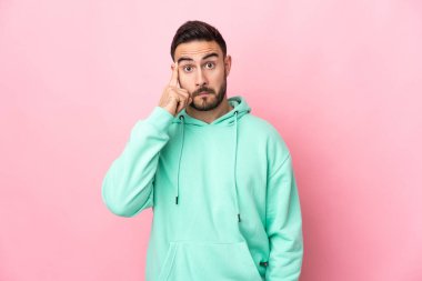 Pembe arka planda izole edilmiş beyaz, yakışıklı bir adam bir fikir düşünüyor.