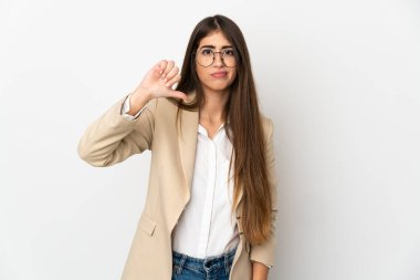 Beyaz arka planda izole edilmiş genç beyaz kadın olumsuz ifade ile baş parmağını aşağı gösteriyor.