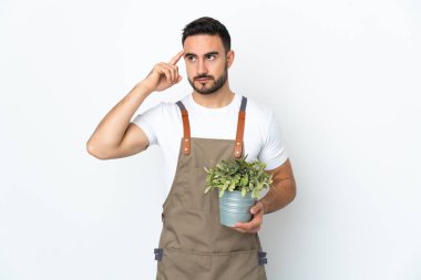 Bahçıvan beyaz arka planda bir bitki tutuyor. Şüpheleri ve düşünceleri var.
