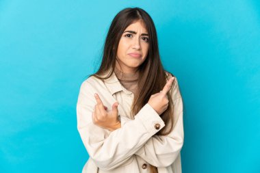 Mavi arka planda izole edilmiş genç beyaz kadın, yan taraftakilerin şüphelerine işaret ediyor.