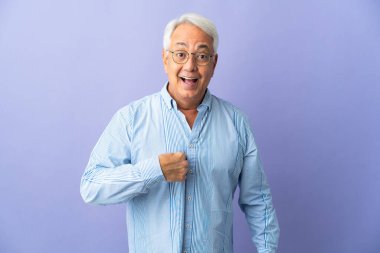 Orta yaşlı Brezilyalı adam mor arka planda izole edilmiş, şaşırmış bir yüz ifadesi var.