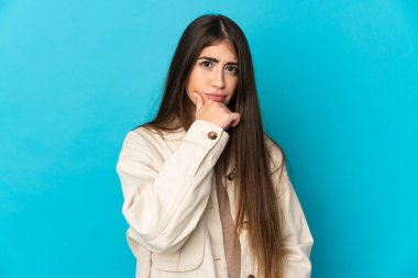 Kafkasyalı genç bir kadın mavi arka planda izole edilmiş. Şüpheleri var.