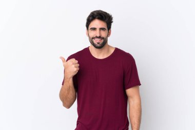 İzole edilmiş beyaz bir geçmişi olan sakallı yakışıklı genç bir adam bir ürün sunmak için kenarı işaret ediyor.