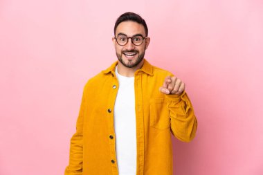 Pembe arka planda izole edilmiş beyaz, yakışıklı genç adam şaşırmış ve ön tarafı işaret ediyor.