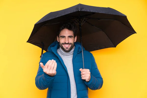 隔離された黄色の背景に傘を持っている男が手を携えて来るように誘う 来てくれて嬉しい — ストック写真