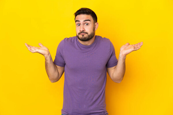 Young caucasian handsome man isolated on yellow background having doubts while raising hands