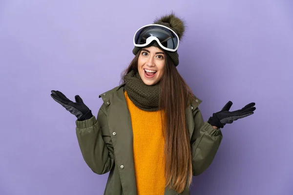 滑雪者高加索女孩与雪板眼镜隔离紫色背景与震惊的面部表情 — 图库照片