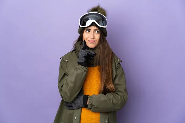 滑雪者高加索女孩与雪板眼镜隔离紫色背景有疑问和思考 — 图库照片