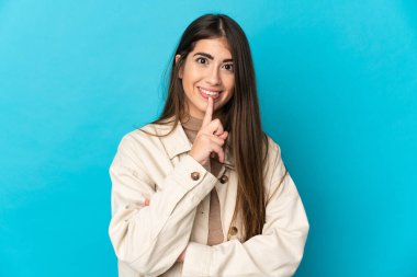 Mavi arka planda izole edilmiş beyaz bir kadın sessiz bir jest işareti gösteriyor. Parmağını ağzına sokuyor.