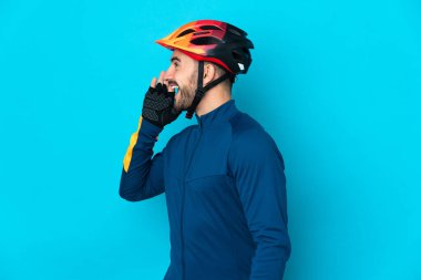 Mavi arka planda izole edilmiş genç bisikletçi ağzı sonuna kadar açık bağırıyor.