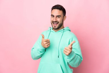 Pembe arka planda izole edilmiş beyaz, yakışıklı genç adam şaşırmış ve ön tarafı işaret ediyor.