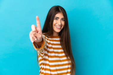Mavi arka planda izole edilmiş genç beyaz kadın parmağını kaldırıyor ve gösteriyor.