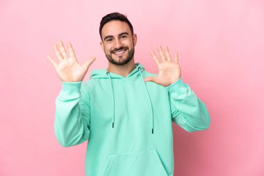 Pembe arka planda izole edilmiş beyaz tenli yakışıklı adam parmaklarıyla ona kadar sayıyor.