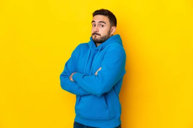 Beyaz tenli yakışıklı adam sarı arka planda izole edilmiş. Omuzlarını kaldırırken şüpheyle hareket ediyor.